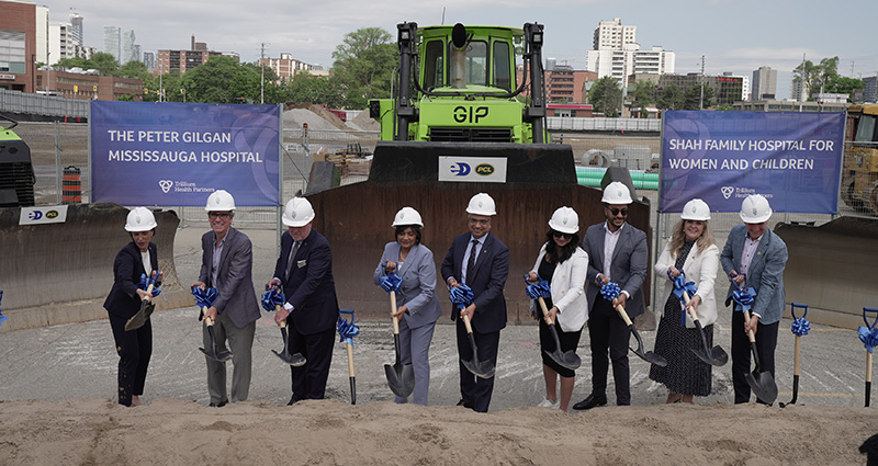 A groundbreaking event scene with several people holding shovels in front of a large sign.